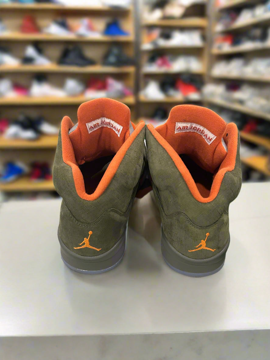 Green and orange sneakers with a brand logo on a white surface, shelves of shoes in the background.