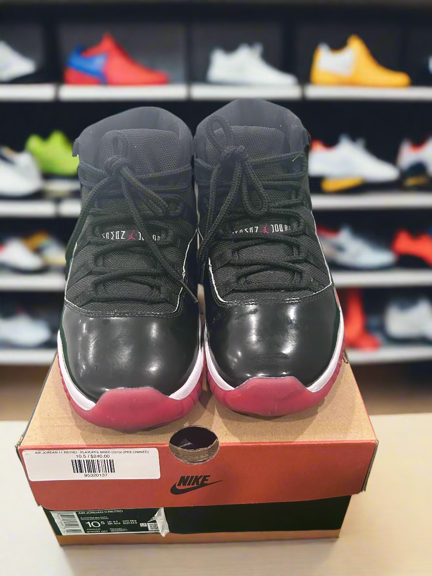 Black high-top sneakers with red soles on a Nike box, against a white and green background.