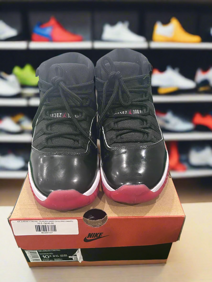 Black high-top sneakers with red soles on a Nike box, against a white and green background.