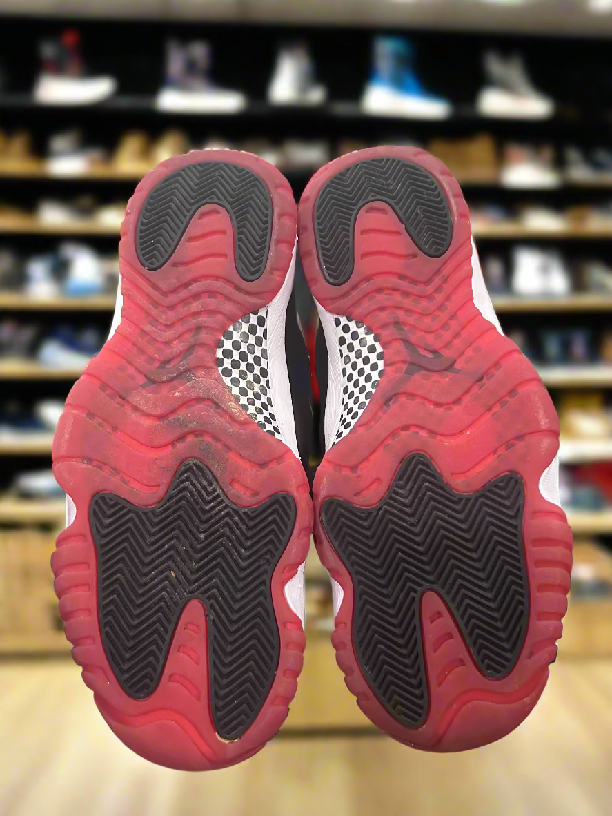 Red and black shoe soles held above a box with a green surface and white wall in the background.