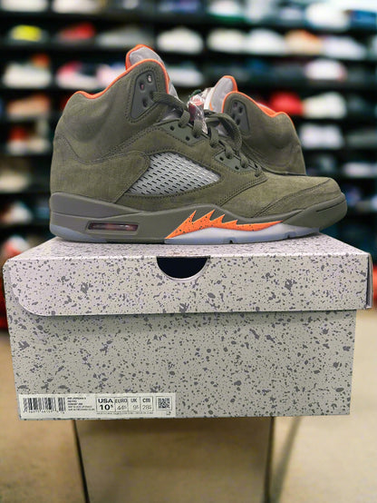 Green sneaker with orange accents on a gray speckled box against a green grass-like surface.